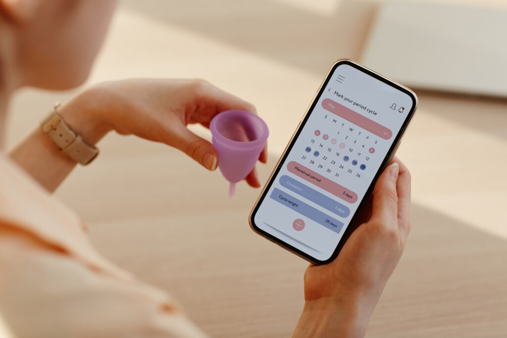 Woman holding a menstrual cup while tracking her menstrual cycle on a phone app.